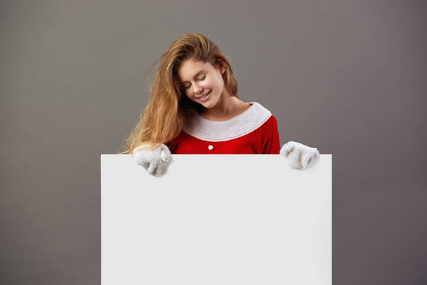 Güzel genç bayan. Noel Baba kırmızı elbise ve beyaz eldiven giymiş onun önünde beyaz tuval gri arka plan üzerinde tutar. - Fotoğraf, Görsel