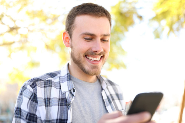 Happy man uses a smart phone walking in a park - Foto, Bild