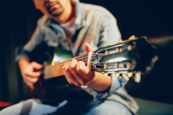 Caucásico talentoso barbudo músico tocando su guitarra acústica y sentado en el sofá. Salón interior
. - Foto, imagen