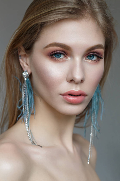 A young girl with long hair, stylish earrings and gentle spring makeup. Beautiful model with shining skin and nude. Portrait made in the studio. wedding look. - Foto, imagen