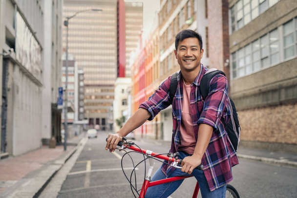 Portrait of a smiling young Asian man in a plaid shirt standing with his bike in the middle of an empty city street - Φωτογραφία, εικόνα