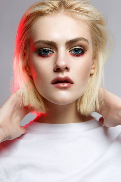 A young girl withblond hair in white t-shirt with a gentle creative make-up. Beautiful model with shining skin and nude. Portrait made in the studio. Color filters. - Фото, зображення