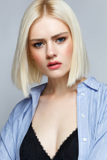 A young girl with blond hair and in a blue shirt with a gentle make-up and blush. Beautiful model with shining skin and nude. Portrait made in the studio. - Foto, immagini