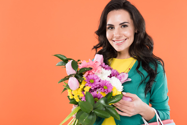 Mulher encaracolado atraente segurando flores e sorrindo isolado em laranja
 - Foto, Imagem