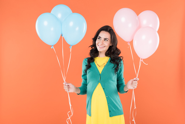 Happy pregnant woman with pink and blue air balloons isolated on orange - Фото, изображение