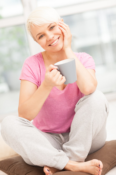 Smiling woman with mug sitting at home while smiling - Foto, afbeelding