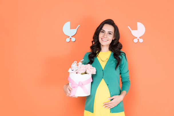 Charming pregnant woman in green cardigan holding flowers on orange background - Photo, Image
