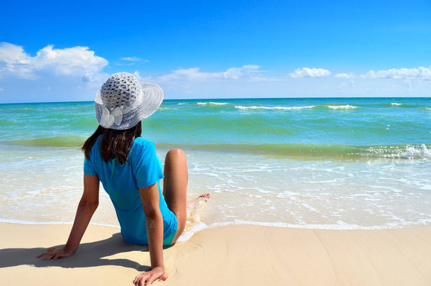 Молода дівчина в білому капелюсі на березі моря. Чистий, піщаний пляж на синьому морі
. - Фото, зображення