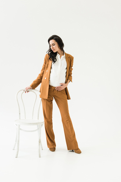 Elegant pregnant woman in suit standing near chair on white background - Photo, Image