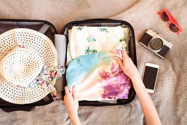 Koffer met ingepakte zomer kleding, een camera, een hoed en sunglas - Foto, afbeelding