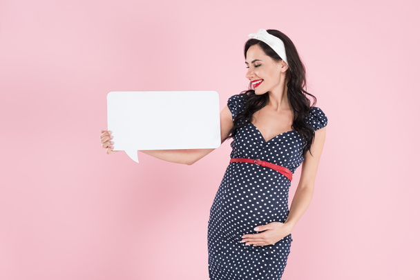 Pretty pregnant woman holding speech bubble and touching belly on pink background - Фото, зображення