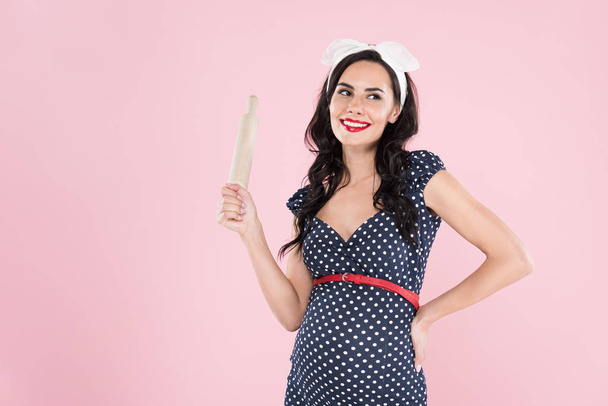 Attractive pregnant young woman holding rolling pin isolated on pink - Photo, image