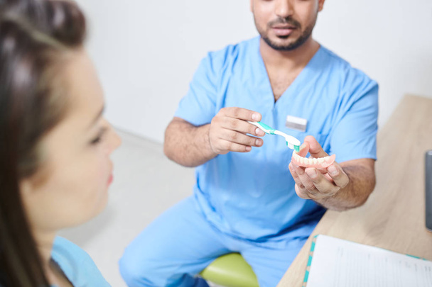 Crop shot of male dentist holding teeth model and explaining tooth brushing technique to unrecognizable patient, copy space - Foto, afbeelding