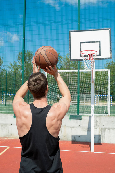 Widok z tyłu portret muskularny młody człowiek rzucanie piłki w obręczy podczas gry w koszykówkę w odkrytym dworze w słoneczny dzień, Kopiuj przestrzeń - Zdjęcie, obraz