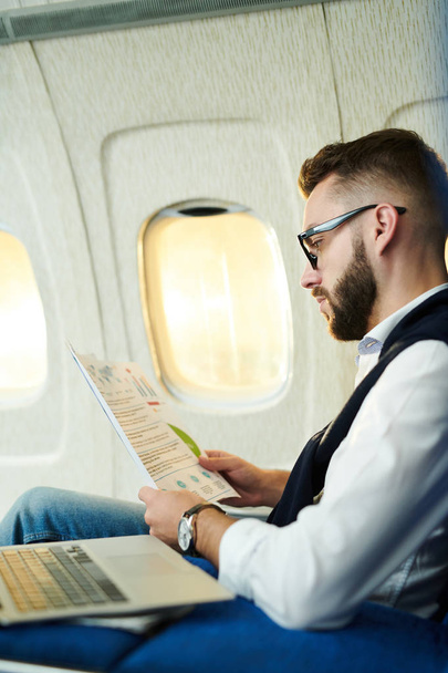 Портрет с боковым видом красивый бизнесмен читает маркетинговые отчеты во время работы в самолете во время длительного перелета, копировать пространство
 - Фото, изображение