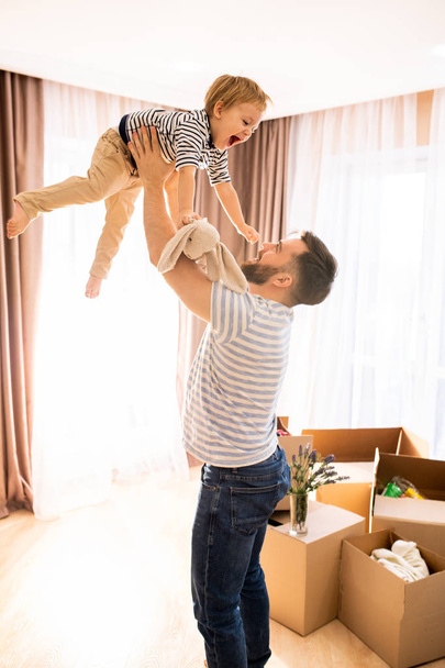 Portrait of happy father playing with son throwing him in the air while enjoying time together at home - Photo, Image