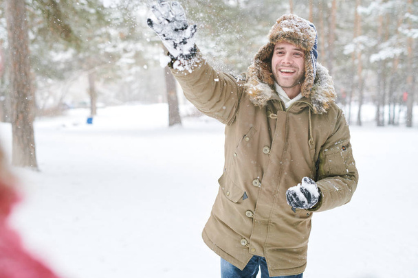 Waist up portrait of handsome young man enjoying snowball fight with friends in beautiful winter forest, copy space - Photo, Image