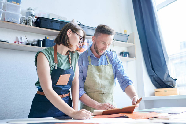 Two tanners, man and woman, standing in apron and working with leather textile - Foto, Imagem