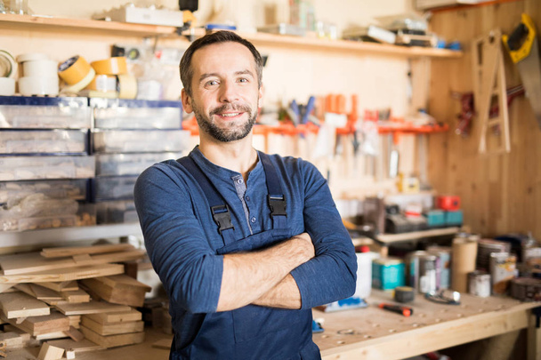 Waist up portrait of mature carpenter looking at camera and smiling while standing with arms crossed in modern joinery, copy space - Fotografie, Obrázek
