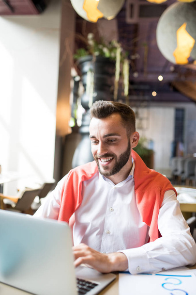 Портрет улыбающегося молодого предпринимателя с ноутбуком во время работы в кафе, копировальное пространство
 - Фото, изображение