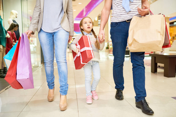 Gewas ouders met papieren tassen lopen in winkelcentrum met klein meisje dragen Kerstcadeaus - Foto, afbeelding