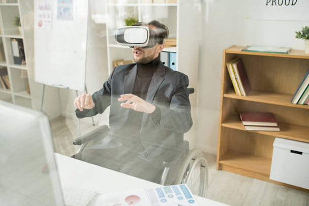 Инвалид-бизнесмен, использующий устройство виртуальной реальности за столом в офисе
 - Фото, изображение