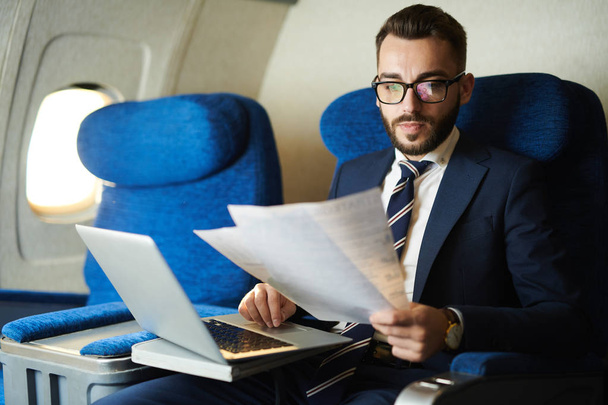 Retrato de belo empresário barbudo lendo documento e trabalhando enquanto desfruta de voo em primeira classe, espaço de cópia
 - Foto, Imagem