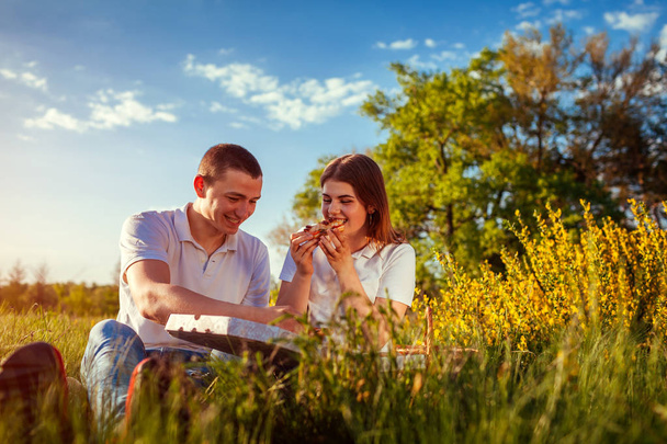 Giovane coppia mangiare pizza e chiacchierare fuori. Donna e uomo che fanno un picnic al tramonto. Stile di vita
 - Foto, immagini