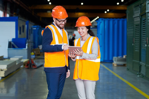 Portrait of female factory worker talking to businessman wearing hardhat while using digital tablet standing in production workshop and using digital tablet, copy space - Photo, image