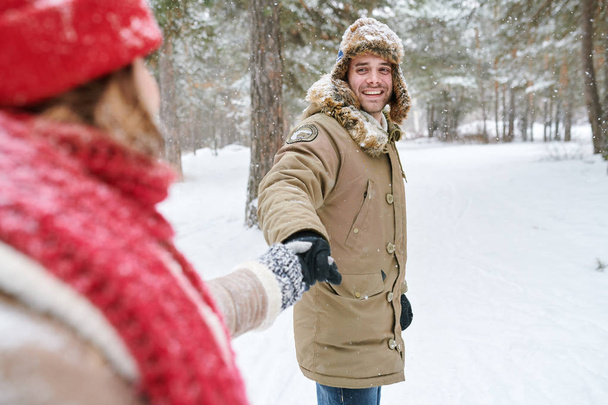 Waist up portrait of handsome young man looking at girlfriend and smiling happily while leading her through beautiful winter park, copy space - Foto, immagini