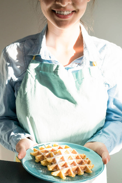 Porträt einer lächelnden Kellnerin, die einen Teller mit leckeren frischen Waffeln im Sonnenlicht hält - Foto, Bild
