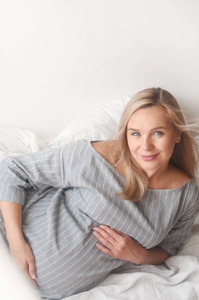 Happy pregnant woman lie on a bed at home - Fotografie, Obrázek