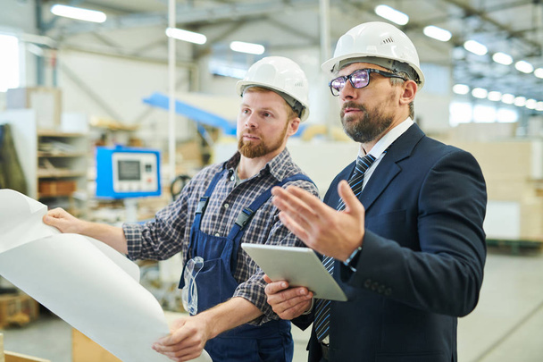 Serious confident business investor in glasses gesturing hand while asking question to young engineer,  businessman visiting factory and talking to engineer - Foto, immagini