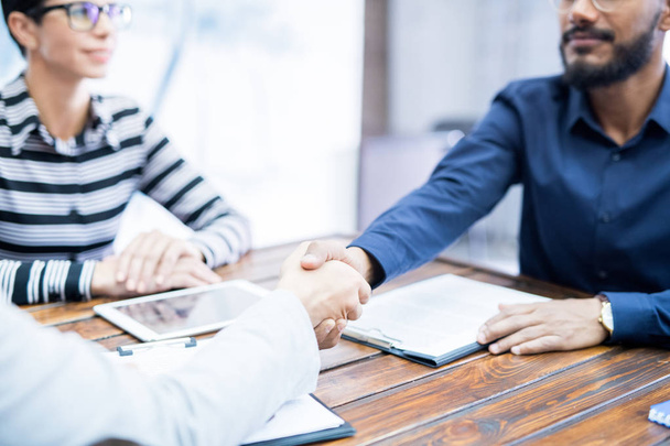 Primo piano di due uomini d'affari seduti a tavola che si stringono la mano durante una riunione in ufficio
 - Foto, immagini