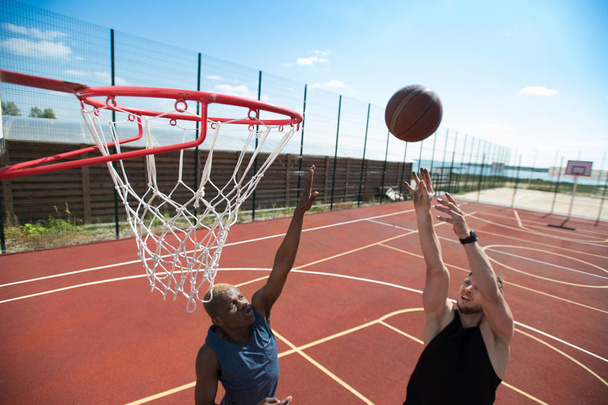 Retrato de jogador de basquete jovem jogando bola na cesta na quadra ao ar livre iluminado pela luz solar, espaço de cópia
 - Foto, Imagem