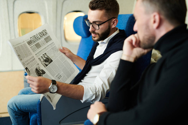 Portret dwóch przystojnych mężczyzn czytania gazety w samolocie korzystających z długiego lotu pierwszej klasy, Kopiuj przestrzeń - Zdjęcie, obraz