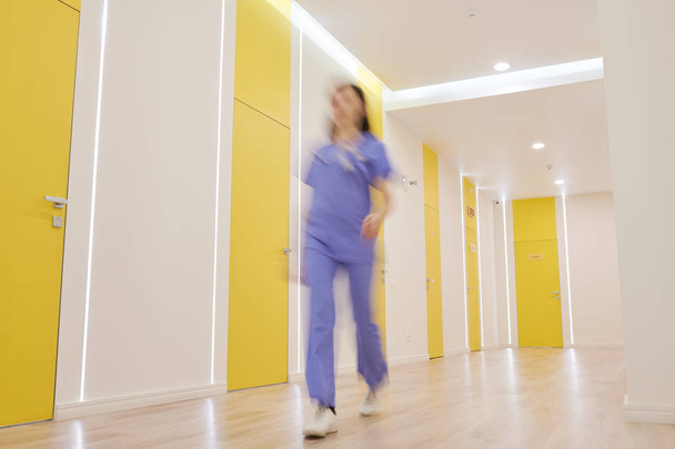 Laaja kulma näkymä käytävällä nykyaikaisella klinikalla, jossa sairaanhoitajan hämärä muoto kävelee, kopioi tilaa
 - Valokuva, kuva