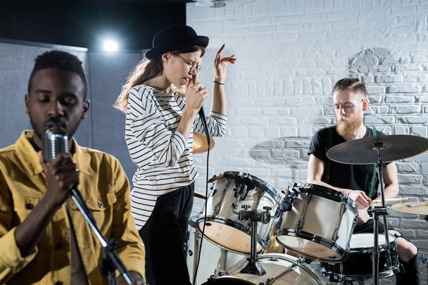 Portret van hedendaagse muziek band presteren op het podium, focus op jonge vrouw zingen naar microfoon, kopieer ruimte - Foto, afbeelding