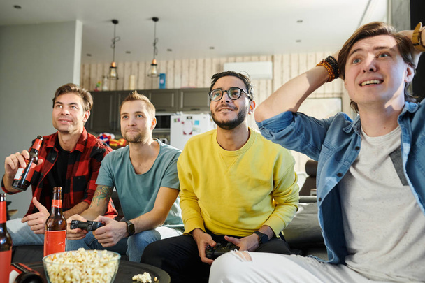 Entusiasmados amigos engraçados se reuniram em casa com cerveja e batatas fritas e jogando videogames na TV
 - Foto, Imagem