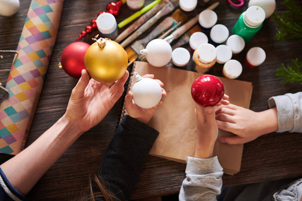 Wysoki kąt zbliżenie dzieci trzyma bombki świąteczne nad drewnianym stole w klasie rzemiosła, Kopiuj przestrzeń - Zdjęcie, obraz