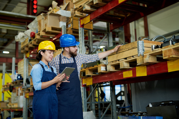 Retrato de dois trabalhadores de fábrica modernos, homem e mulher, vestindo hardhats fazendo inventário de pé por prateleiras em armazém, espaço de cópia
 - Foto, Imagem