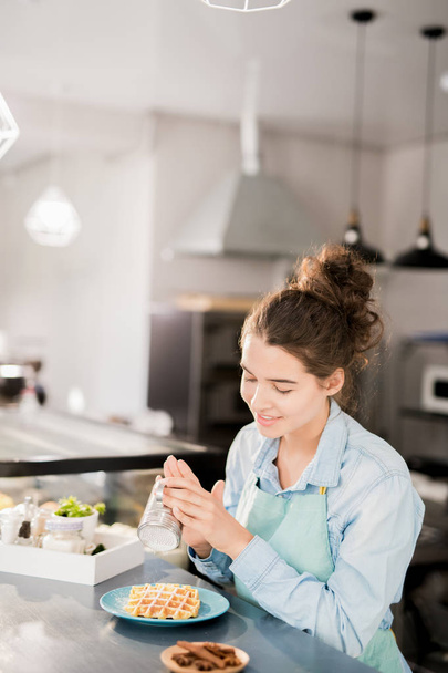 Портрет усміхненої молодої жінки, яка поливає корицю і цукрову пудру на свіжі вафлі, готуючи замовлення в маленькому кафе, копіювати простір
 - Фото, зображення
