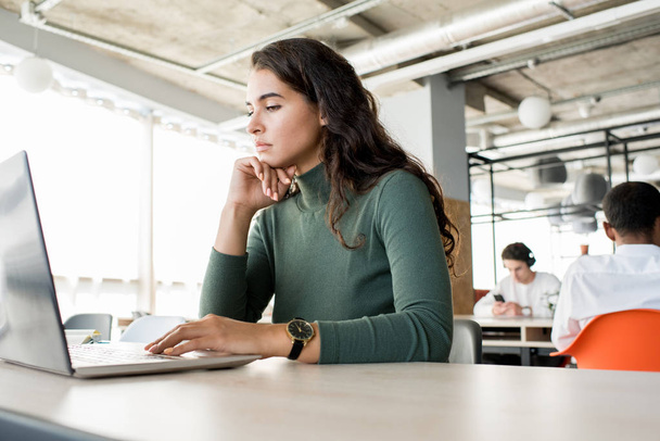 Портрет задумчивой молодой женщины, использующей ноутбук во время работы в открытом офисе, копировальное пространство
 - Фото, изображение