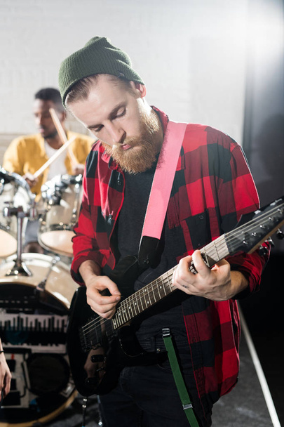 Cintura até retrato de homem barbudo contemporâneo tocando guitarra durante o ensaio da banda em estúdio
 - Foto, Imagem