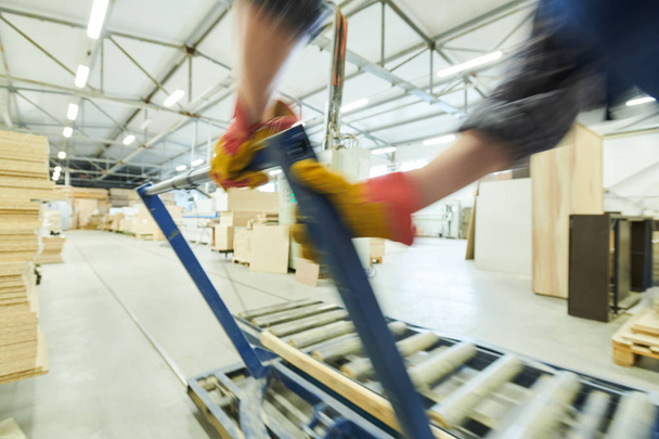 Close-up de trabalhador irreconhecível ajustando alça de metal enquanto regula transportador de rolos na fábrica de móveis
 - Foto, Imagem