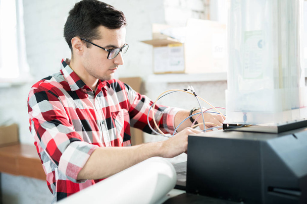 Serious busy handsome young male engineer in glasses repairing printer in office of printing company and checking ink cables - Φωτογραφία, εικόνα