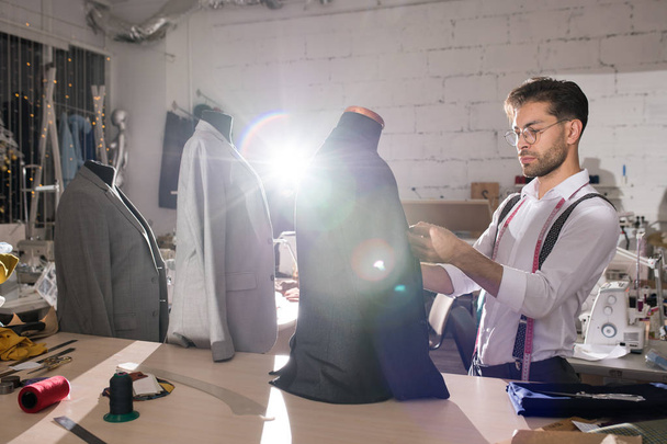 Portret van knap Tailor fitting formele jassen op mannequins in atelier studio verlicht door gedimd licht, kopieer ruimte - Foto, afbeelding