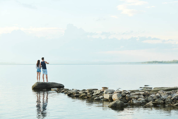 Rückansicht eines jungen Paares, das auf Steinen steht und die schöne Aussicht genießt - Foto, Bild