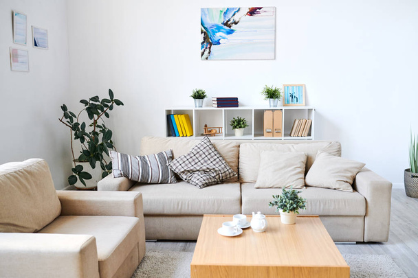 Современный интерьер гостиной с абстрактным рисунком и сертификатами в рамах на стенах: удобный диван и кресло возле кофейного столика
 - Фото, изображение