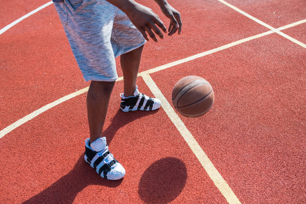 Low section portrait of unrecognizable African man leading ball while playing basketball in outdoor court, copy space - Foto, Imagem